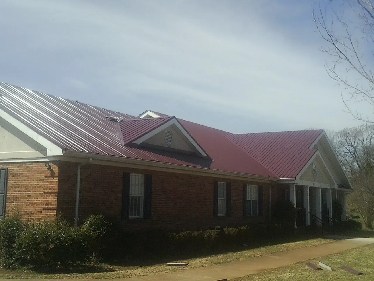 Red metal roof with gabled entries on a long brick building, from a Hail Damage Roof Repair job in Decatur