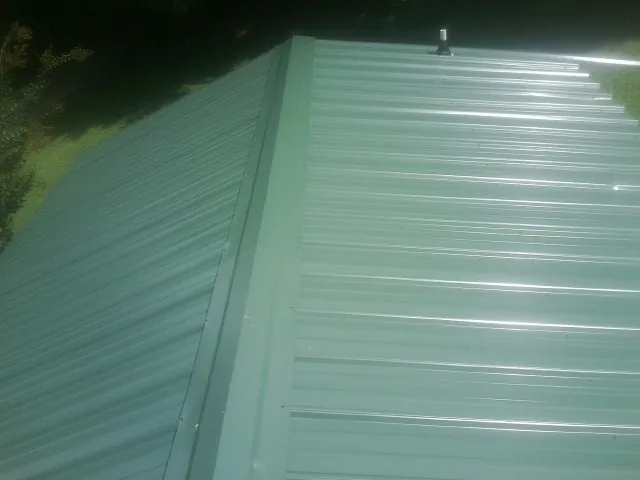 New green metal panels meeting at the ridge of a roof — Flat Roof Repair work by our crew in Decatur