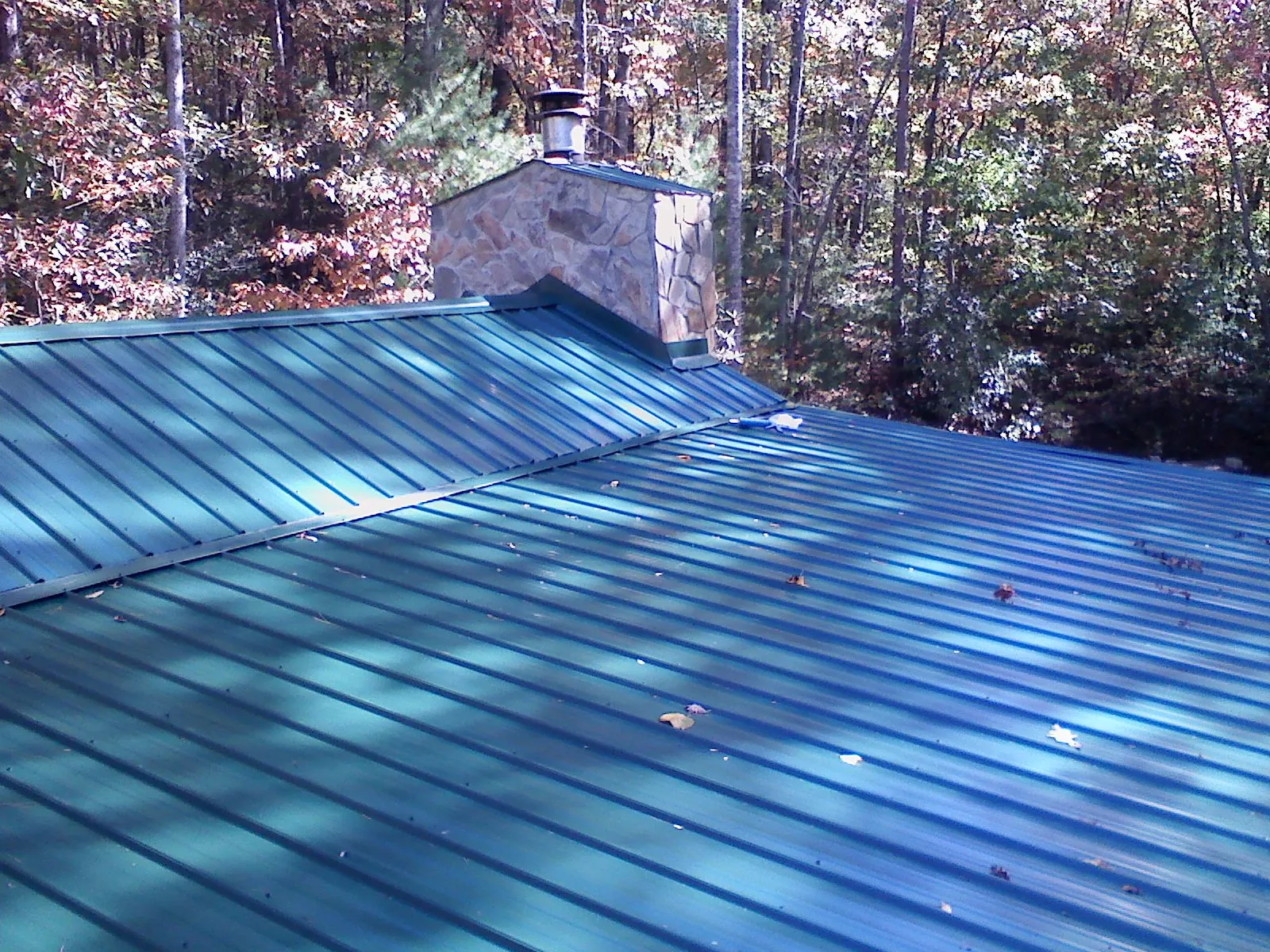 New green metal roof and stone chimney surrounded by autumn woods in Decatur