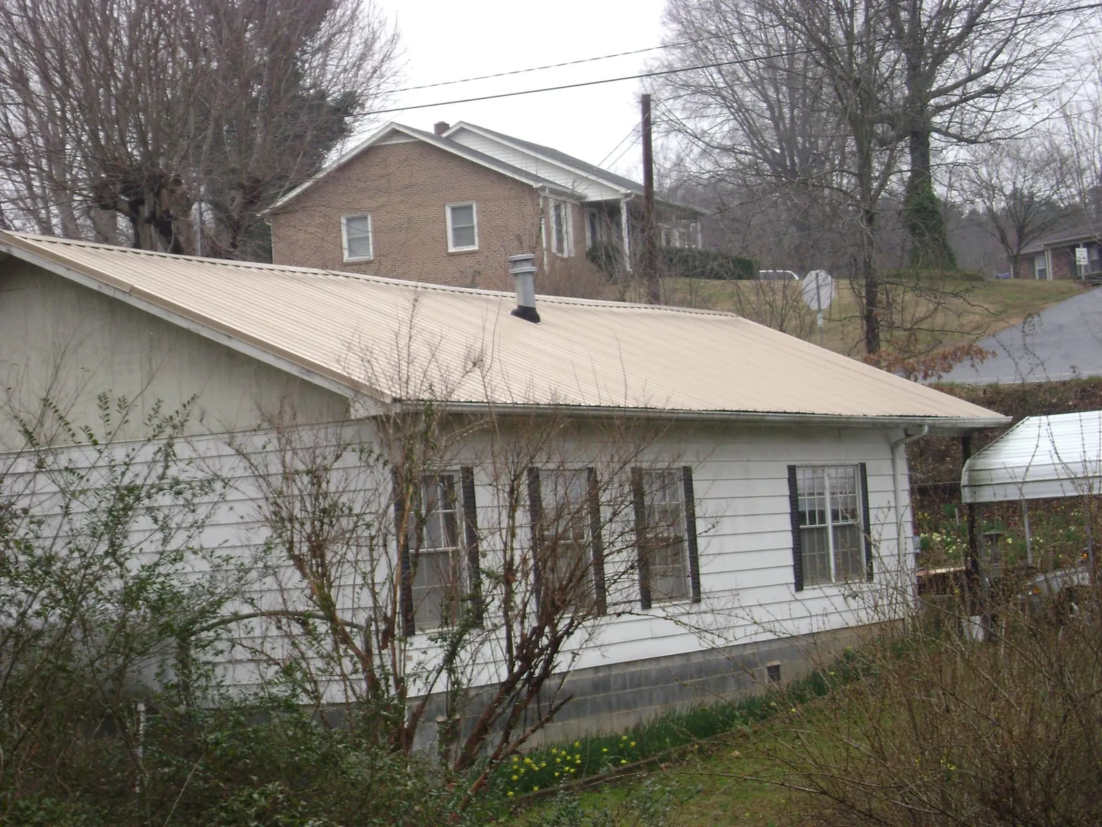 Tan metal roof on a white sided house set into a hillside — Commercial Roofing by Roofing Brothers in Decatur